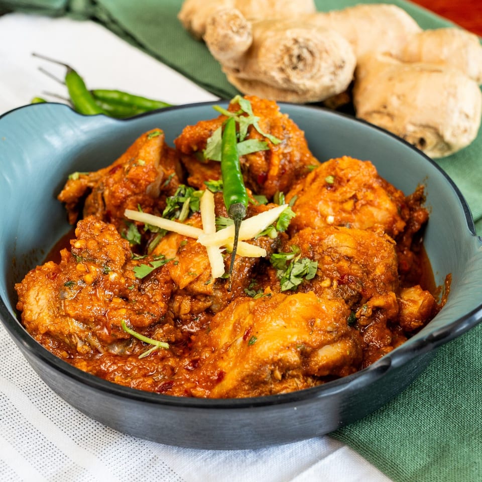 Halal chicken curry in a blue bowl, garnished with green chilies and ginger, on a green cloth.