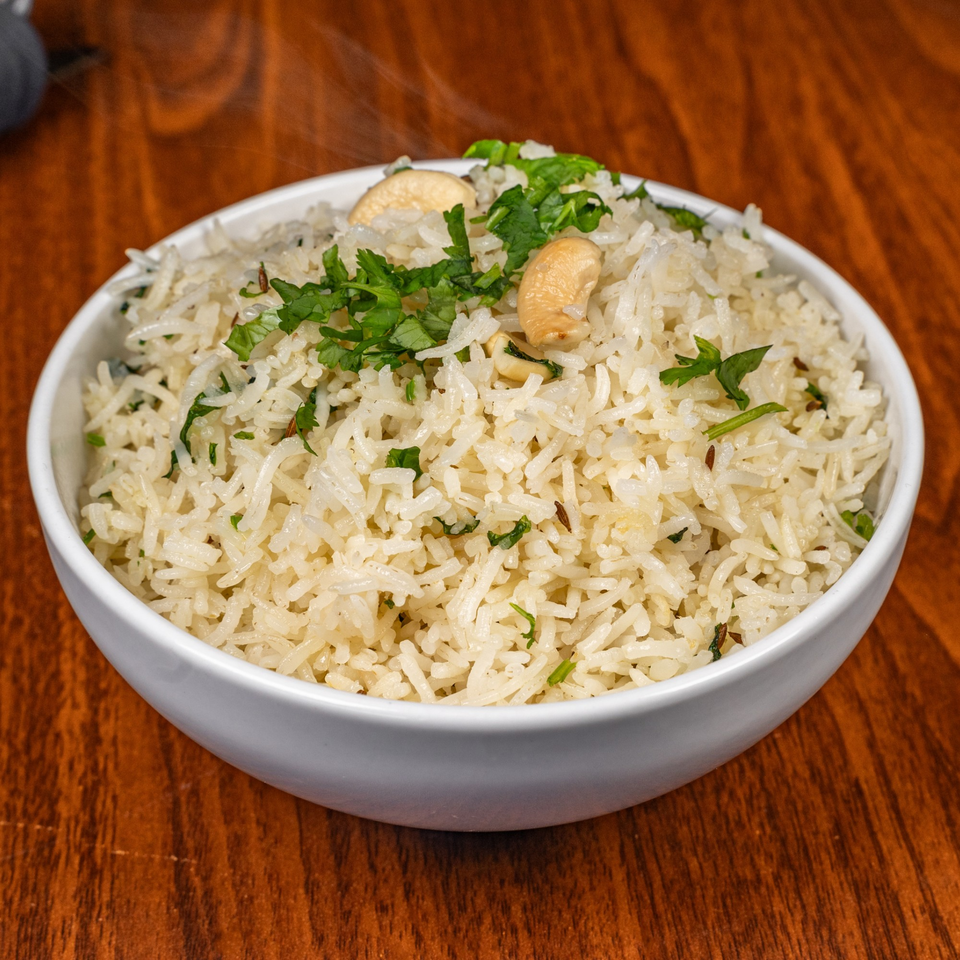 Steaming white rice with cashews and fresh cilantro in a white bowl on a wooden table.