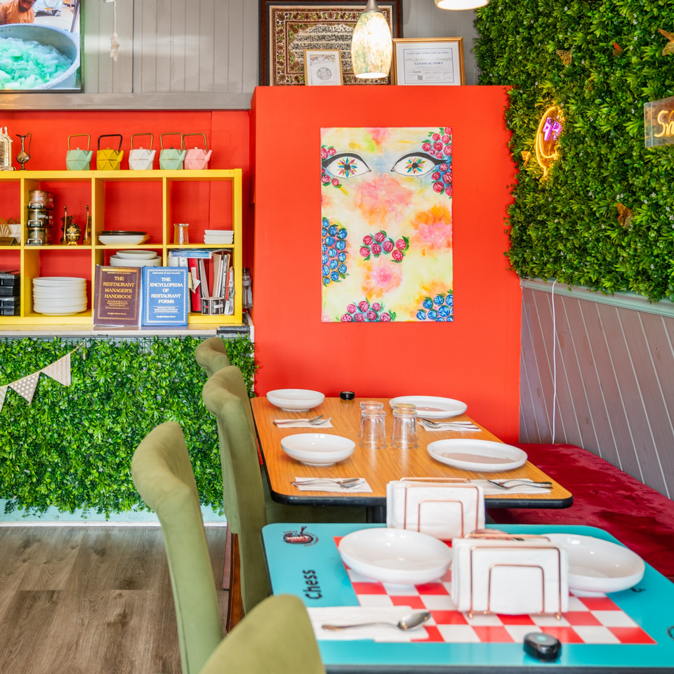 Colorful Suma's Kitchen interior with set tables, a vibrant floral painting, and green wall decor.