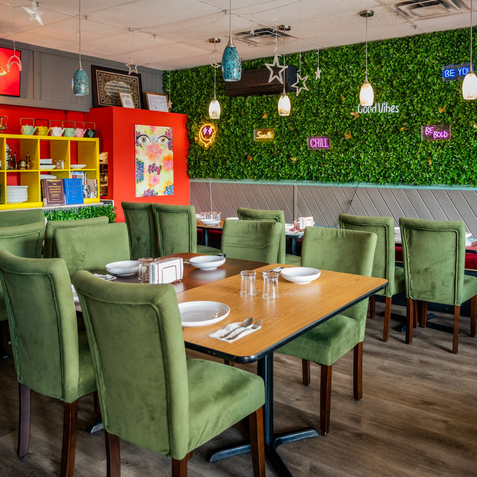 Interior of Suma's Kitchen with green chairs, wooden tables, and a vibrant green wall with neon signs.