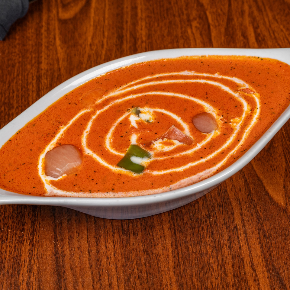A white oval dish filled with orange curry, garnished with white cream swirls and green peppers.