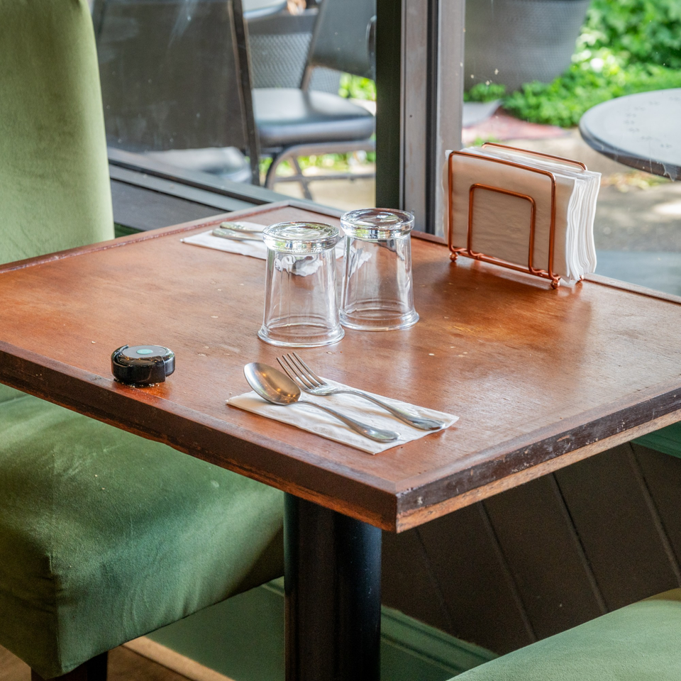 A set table at Suma's Kitchen with green chairs, glasses, silverware, and a napkin holder.