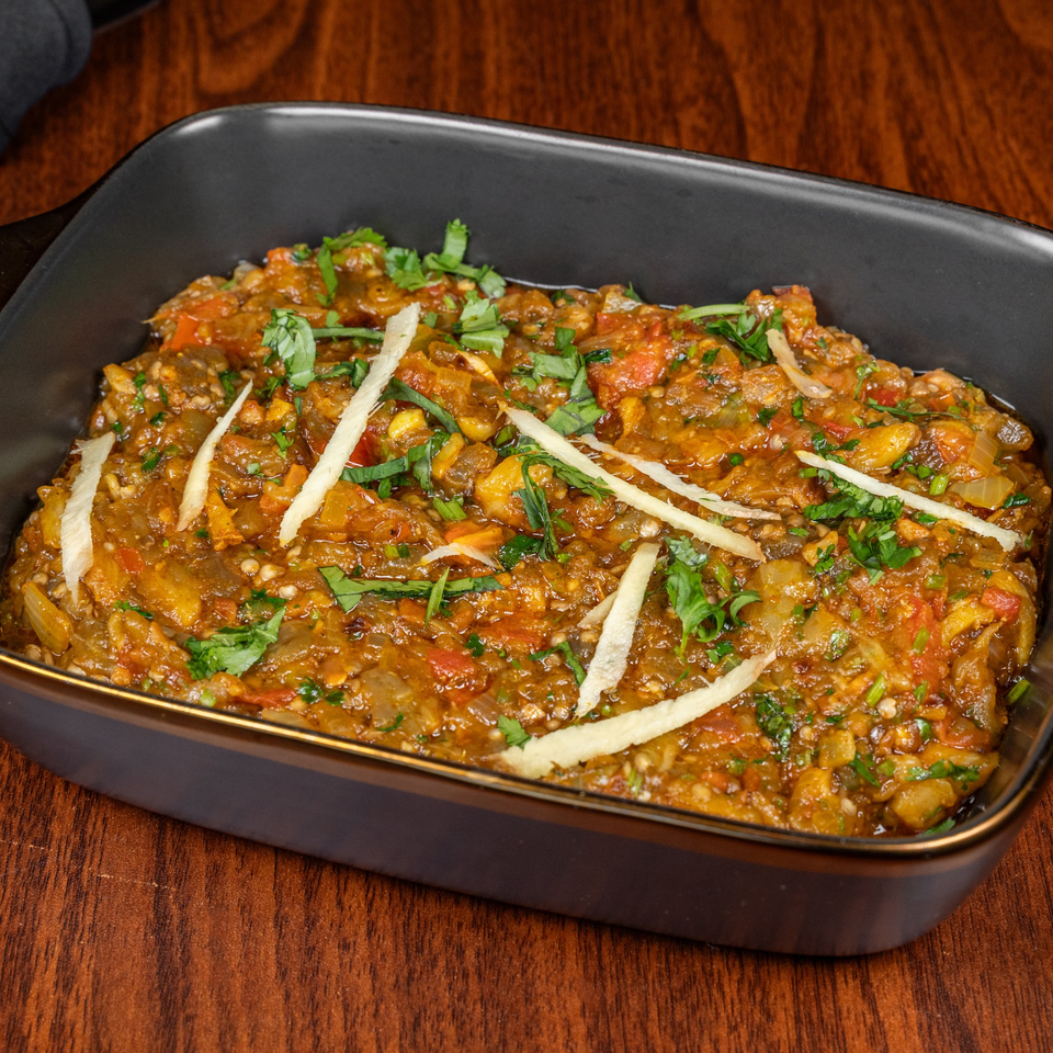 Suma's Kitchen's halal eggplant curry, garnished with fresh cilantro and ginger, in a black dish.