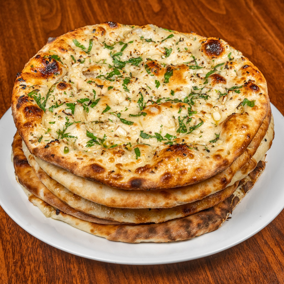Stack of five golden-brown garlic naan breads, garnished with herbs, on a white plate.