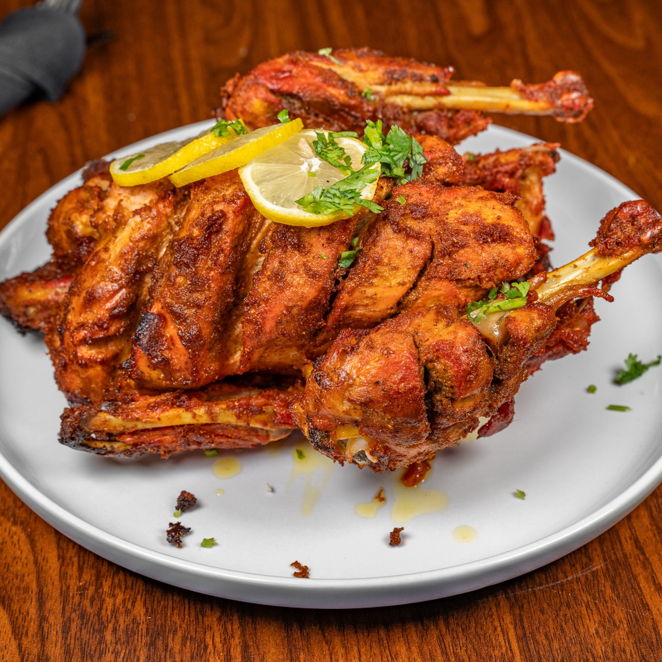 Whole roasted chicken, garnished with lemon slices and fresh parsley, on a white plate.